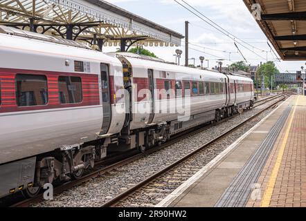 A line of railway carriages stand near a 19th Century historic canopy. An iron bridge is in the distance and a sky with cloud is above. Stock Photo