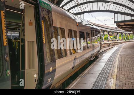 A line of railway carriages stand near a 19th Century historic canopy. The carriage door is open and a yellow line curves into the distance. Stock Photo