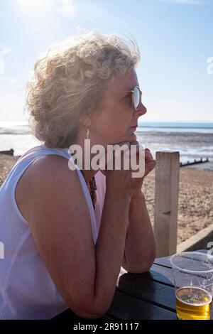 Whitstable North Kent , England UK - Mature woman visitor look relaxed sitting in the late afternoon sunshine in summer Stock Photo