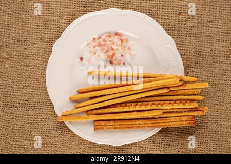 Straw is a bakery product. A few straws with a white plate with salt on a jute cloth, macro, top view. Stock Photo