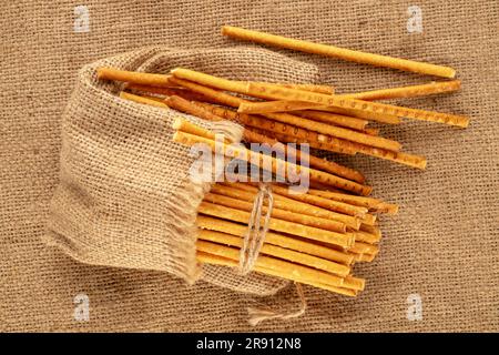 Straw is a bakery product. Several straws with jute bag on jute canvas, macro, top view. Stock Photo