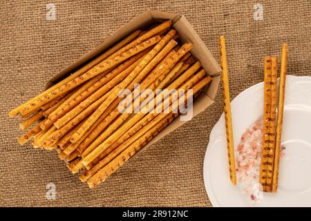 Straw is a bakery product. Several straws with paper plate and salt plate on jute cloth, macro, top view. Stock Photo