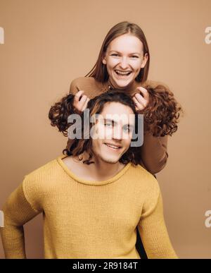 Funny time together. Joyful moments in pairs. Cheerful girl holding curly hair of boyfriend makes him funny hairstyles Stock Photo