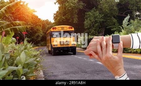 Smart watch on hand on background of yellow bus, checking time of departure and arrival of public buses in tropical country. Stock Photo