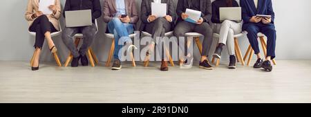 Legs of unrecognizable business people sitting on chairs in a row with resumes and laptops. Stock Photo