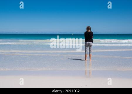 A woman with trousers rolled up enjoys the water and sand on Scarborough Beach in Perth Australia Stock Photo