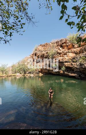 A woman in a bikini checks the water at a swimming hole in the outback near the Gibb River Road in Western Australia in Australia Stock Photo