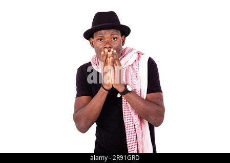 surprised young man wearing hat and scarf, covering mouth with his hands. Stock Photo