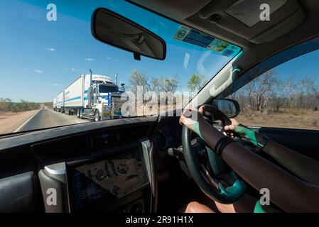 A female drives a car along an Australian Highway as a large road train comes the opposite direction Stock Photo