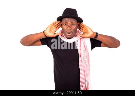 young man wearing a hat and scarf holding both hands on his ear for better listening. Stock Photo