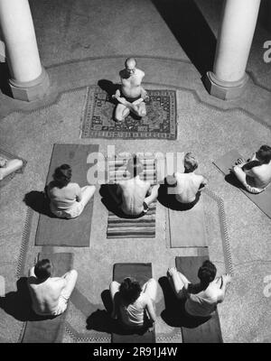 United States: December 2, 1949 A yoga class being held in a  hall where students sit attentively on their mats as Yogi Bittner demonstrates by tying himself in knots. Stock Photo