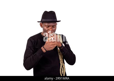 a handsome businessman in a black embroidered shirt standing on a white background lighting a cigarette using a lighter Stock Photo