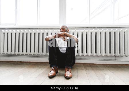 Thoughtful man sitting on hardwood floor near heater at home Stock Photo