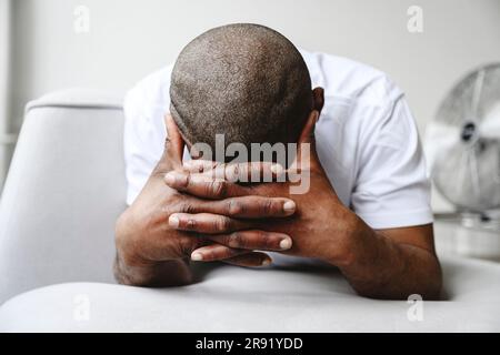 Depressed man with hands clasped leaning on sofa at home Stock Photo
