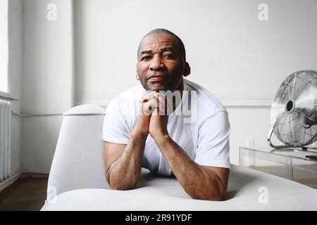 Mature man with hands clasped leaning on sofa at home Stock Photo