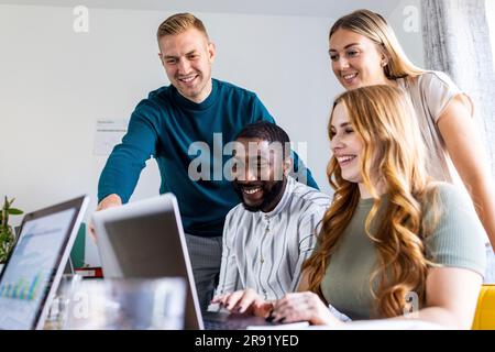 Smiling multiracial colleagues using laptop together at desk in office Stock Photo