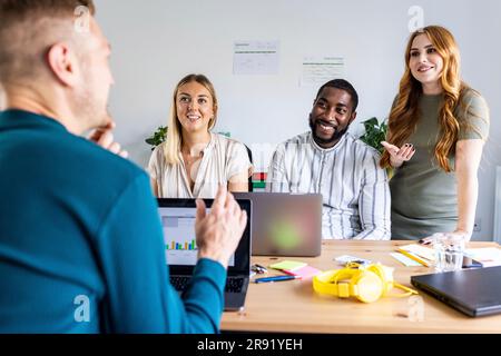 Young businessman talking to smiling colleagues in meeting at office Stock Photo