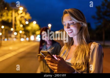 Smiling woman using smart phone with friend in background Stock Photo