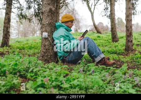 Man using tablet PC connected with outlet on tree trunk Stock Photo