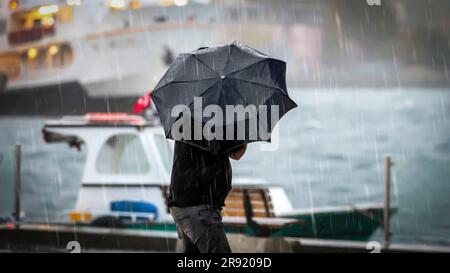 A man with an open umbrella in hand stands on a wooden boat dock in a heavy rain Stock Photo