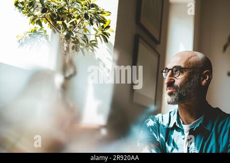 Thoughtful man looking out of window at home Stock Photo