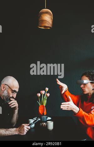 Woman wearing virtual reality headset sitting with man using tablet PC Stock Photo