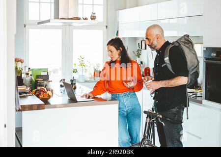 Woman using laptop by man standing with bicycle at home Stock Photo