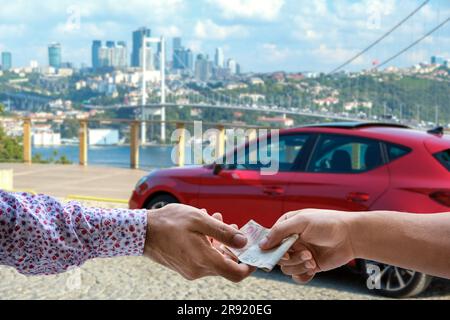 Two businessmen standing in front of a red car in an urban setting, exchanging currency Stock Photo