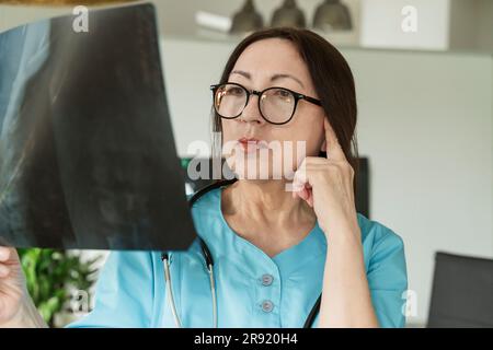 Doctor wearing eyeglasses examining X-ray at medical practice Stock Photo
