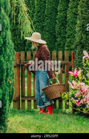 Woman with basket full of logs closing gate in garden Stock Photo