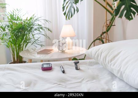 Glucometer and insulin by pillow on bed at home Stock Photo