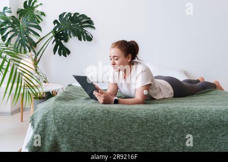 Woman with diabetes using tablet PC lying on bed at home Stock Photo