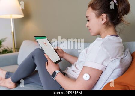 Woman using tablet PC with diabetes glucose sensor on arm at home Stock Photo