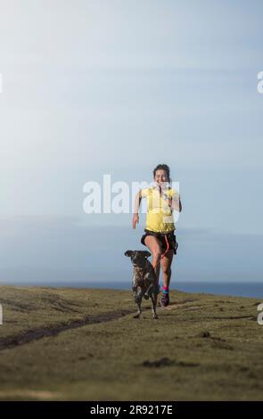 Woman practicing canicross with dog on grass Stock Photo