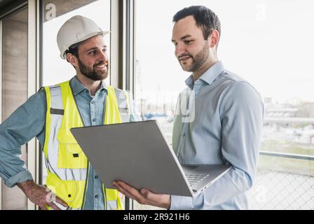 Smiling building contractor looking at architect holding laptop Stock Photo