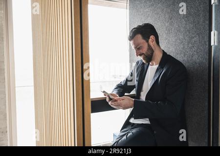 Smiling businessman text messaging through smart phone at office Stock Photo