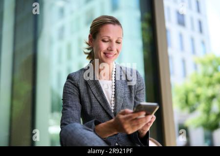 Smiling businesswoman text messaging through smart phone Stock Photo