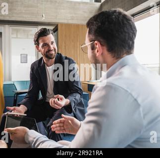 Smiling businessman and colleague discussing at workplace Stock Photo