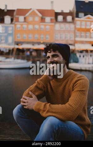 Young man sitting at harbor in front of buildings in city Stock Photo