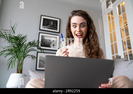 Excited young woman showing pregnancy testing kit on video call over laptop Stock Photo