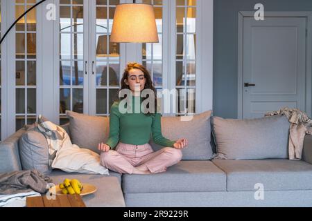 Young woman meditating on sofa at home Stock Photo