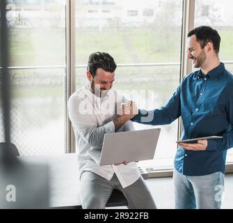Colleagues laughing and holding hands in office Stock Photo