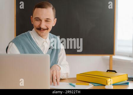 Smiling man sitting in classroom looking at laptop Stock Photo