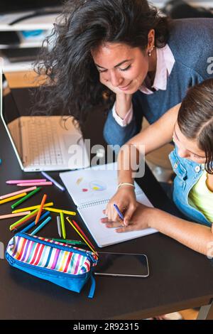 Freelancer mother assisting daughter drawing in notebook at table Stock Photo