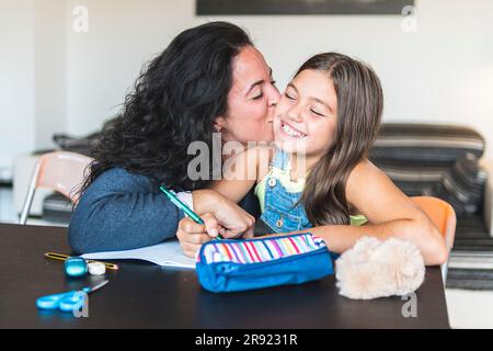Mother kissing daughter doing homework Stock Photo