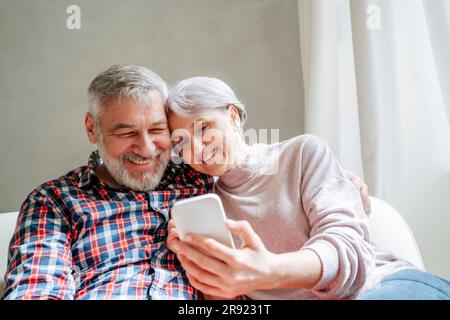 Smiling mature couple using smart phone sitting at home Stock Photo