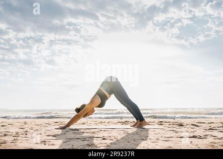 Woman practicing Adho mukha svanasana pose at beach Stock Photo