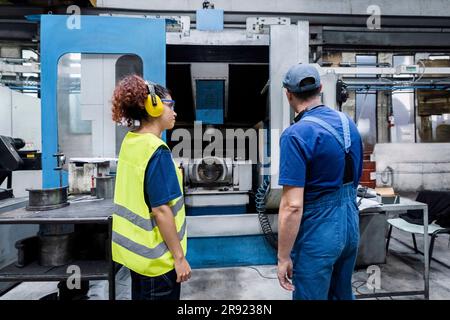 Maintenance engineer examining coworker working on machinery in modern factory Stock Photo
