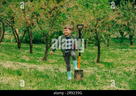 Smiling boy with shovel standing in front of trees at garden Stock Photo