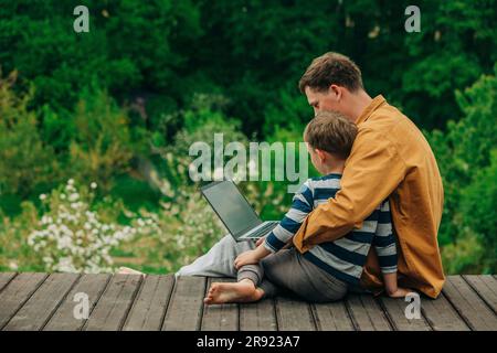 Son with father using laptop on boardwalk Stock Photo